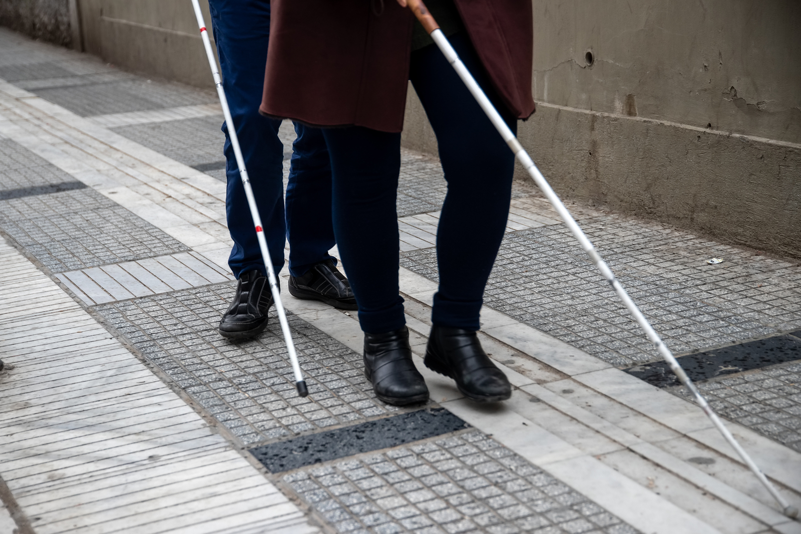A blind man and woman walking together, both are using white mobility canes.