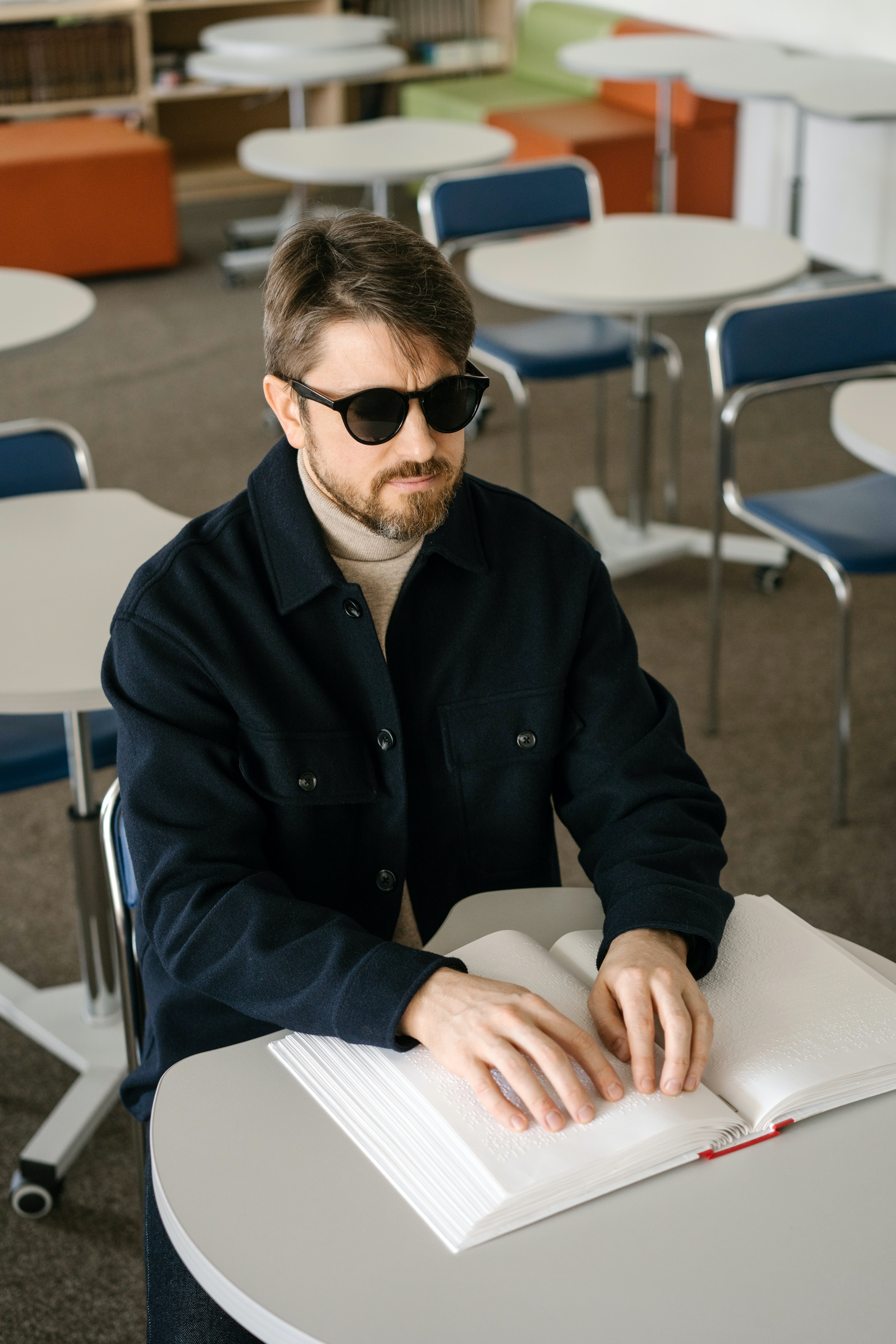 A young man sitting in a classroom reading a braille document.