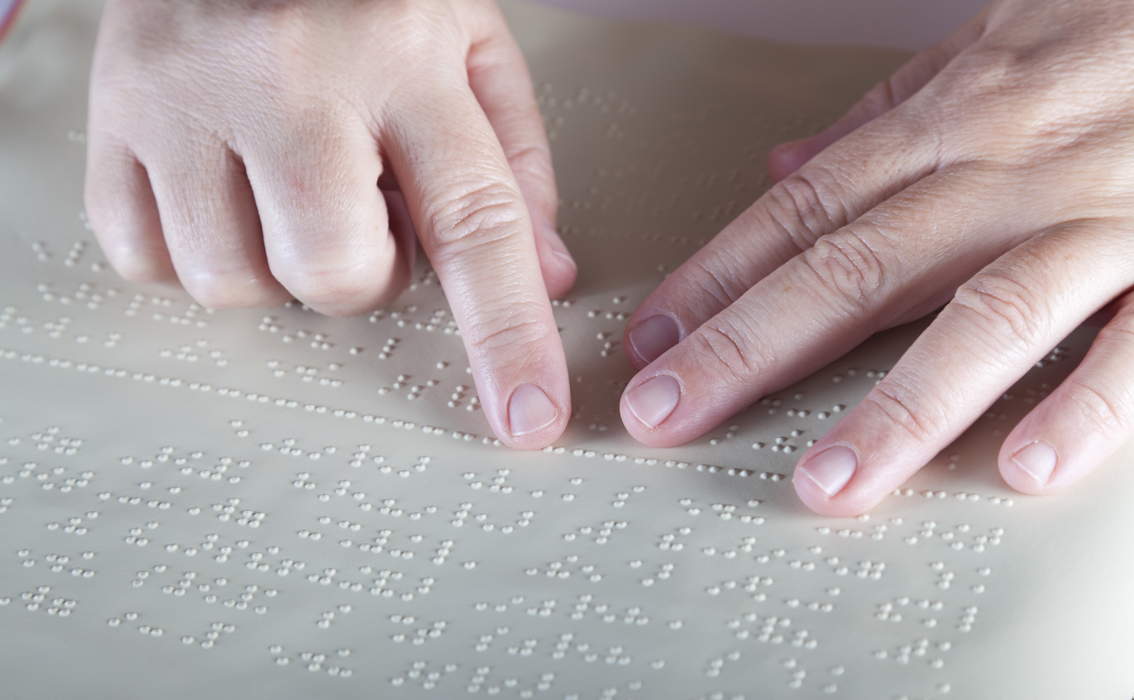 Hands reading a sheet of paper, with braille embossed on it.